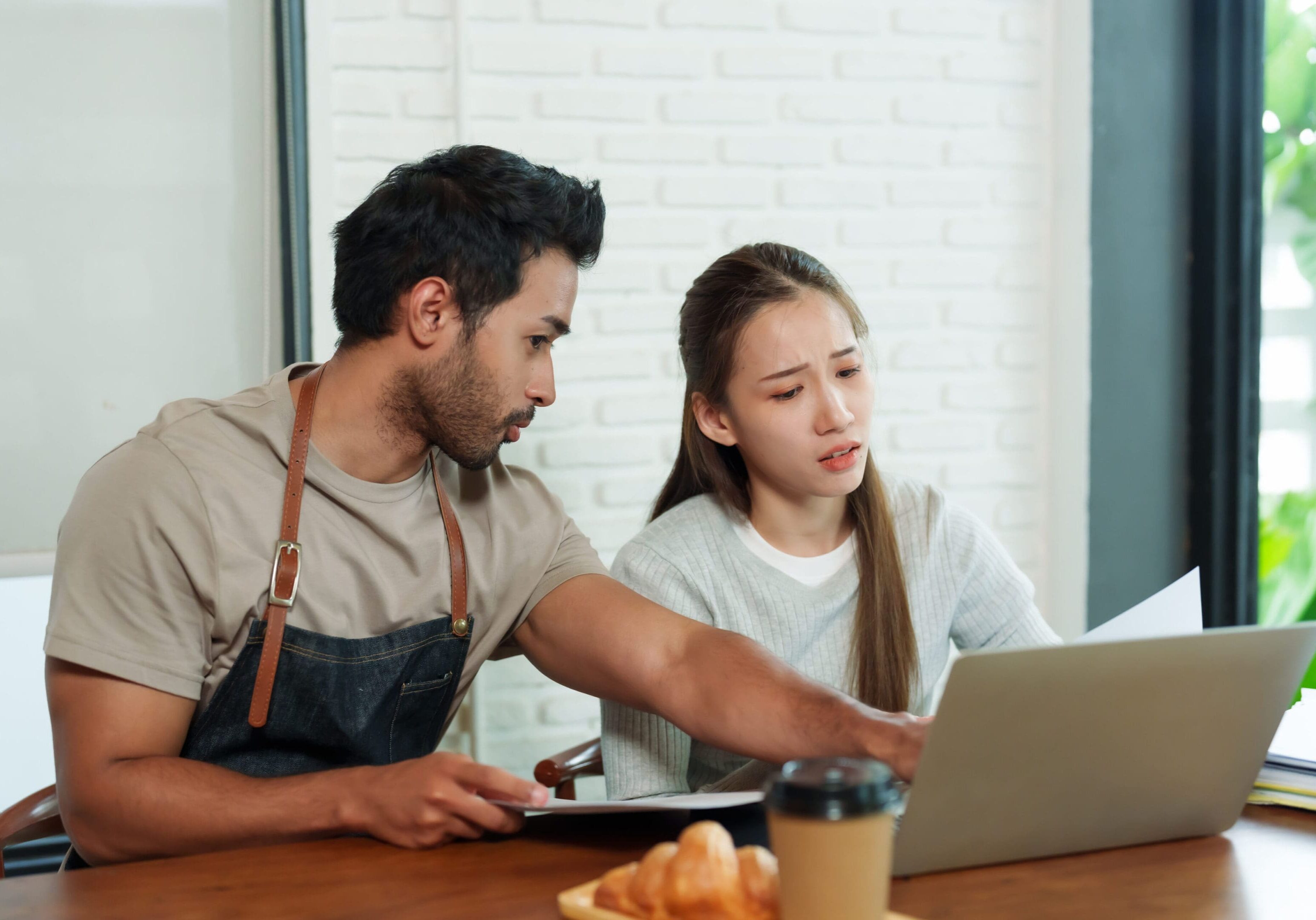 A man and woman sitting at a table looking at a laptop.